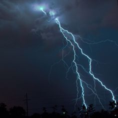 a lightning bolt is seen in the sky above some trees and power lines at night