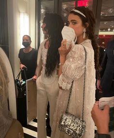 a woman is standing in front of a mirror drinking from a paper cup while wearing white