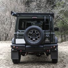 the rear end of a black jeep parked on top of a dirt field next to trees