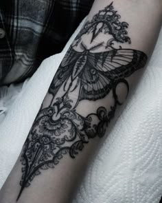 a black and white photo of a butterfly tattoo on the left arm, with an intricate design