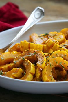 a white bowl filled with cooked squash on top of a wooden table next to a spoon