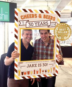 two men standing next to each other holding up a sign with cheers and beers written on it