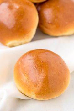 four rolls sitting on top of a white napkin next to some other food items in the background