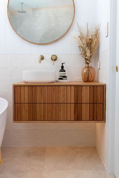 a white bath tub sitting next to a wooden cabinet under a round mirror in a bathroom