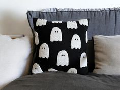 a black pillow with white ghost faces on it sitting on a gray couch next to pillows