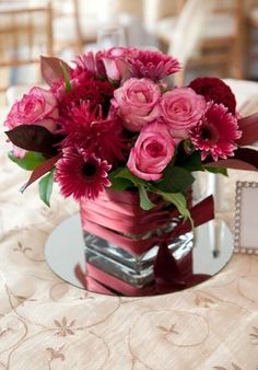 a vase filled with pink flowers sitting on top of a table next to a mirror