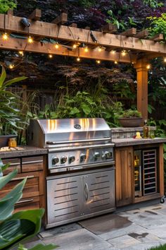 an outdoor kitchen with lights strung over the grill and seating area, surrounded by greenery