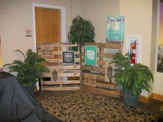 a room with several wooden pallets and plants in the corner, along with posters on the wall