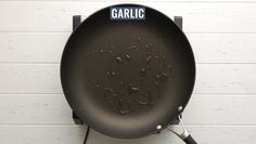 a frying pan with the word garlic on it hanging from a hook against a white brick wall