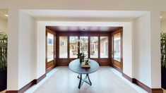 a room with a table, potted plants and two large doors leading to the outside