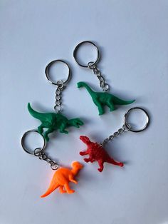 three plastic dinosaur keychains on a white surface, one is orange and the other is green