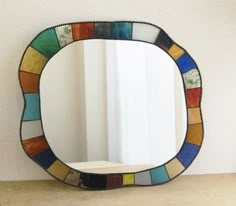 a colorful mirror sitting on top of a counter next to a white wall and window