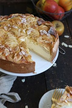 a pie on a plate with a slice missing from it and apples in the background