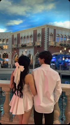 a man and woman standing next to each other in front of a building with a sky background