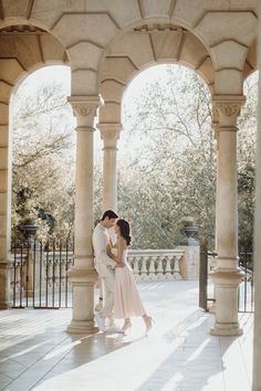 an engaged couple kissing in front of pillars