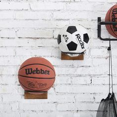 three basketballs are hanging on the wall next to two net balls and a wire bag