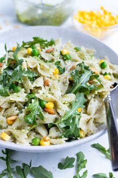 a white bowl filled with pasta salad next to corn and parsley on the side