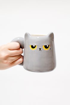 a hand holding a gray cat mug with yellow eyes