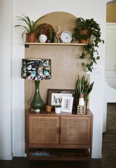 a shelf with plants and pictures on top of it next to a wall mounted clock