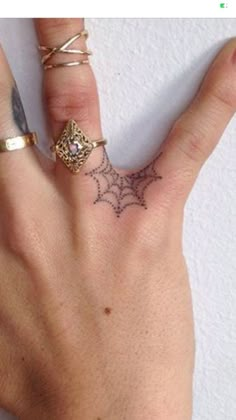 a person's hand with two rings on it and a spider web tattoo on the middle finger