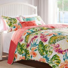 a bed with floral comforter and pillows in a bedroom next to a white dresser