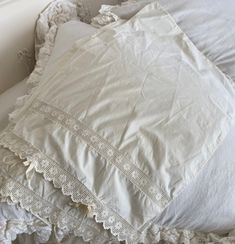 an unmade bed with white linens and lace on the pillowcase is shown