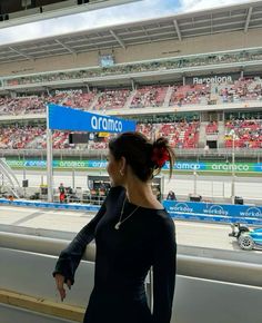 a woman standing in front of a race track looking out at the stands and cars