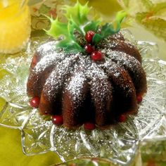 a bundt cake on a glass plate covered in powdered sugar and holly berries