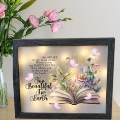 an open book with flowers in vase next to it on a wooden table and light up frame