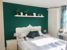 a bedroom with green walls, white bedding and two plants on the headboard