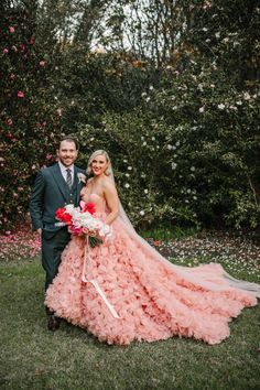 a bride and groom pose for a wedding photo in front of pink flowers on the grass