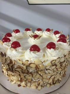 there is a cake with white frosting and cherries on the top, topped with nuts