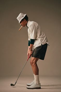 a man in white shirt and shorts holding a golf club while standing next to a ball