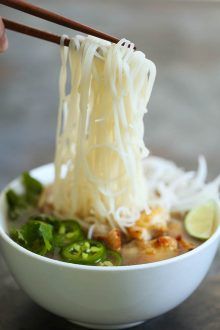 someone is holding chopsticks above a bowl of noodles and vegetables with sauce on the side