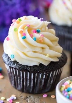 a cupcake with white frosting and sprinkles on it sitting next to a bowl of confetti