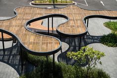 an artisticly designed wooden bench sits in the middle of a parking lot with trees and bushes around it