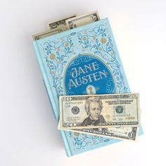 a stack of one hundred dollar bills sitting on top of a blue book with jane aushen written on it