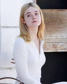 a woman sitting on top of a wooden bench next to a wall holding a brown purse