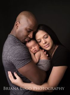 a man and woman holding a baby in their arms, while they are looking at the camera