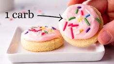 a person holding a pink frosted donut on top of a white plate