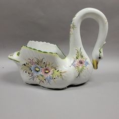 a white swan shaped vase with flowers painted on it