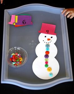 a snowman made out of buttons sitting on top of a tray next to a plastic bowl