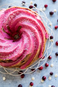 a cake with pink icing and white sprinkles sits on a wire rack