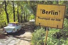 an old car driving down a dirt road next to a yellow sign that says berlin