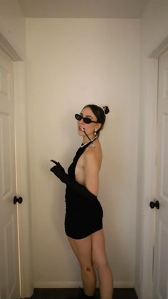 a woman in a black dress and sunglasses posing for the camera with her hands behind her back