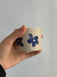 a hand holding a white cup with blue flowers on it