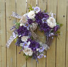 a wreath with purple and white flowers hanging on a wooden fence