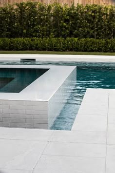 an empty swimming pool surrounded by hedges and trees in the backround, with water running through it