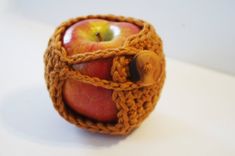 an apple in a knitted basket with a wooden button on the side and two apples inside