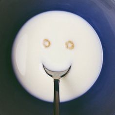 a smiley face drawn on the side of a spoon in a bowl with milk and two gold rings sticking out of it